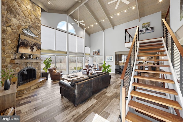 living room featuring a ceiling fan, wood tiled floor, a stone fireplace, stairs, and wood ceiling