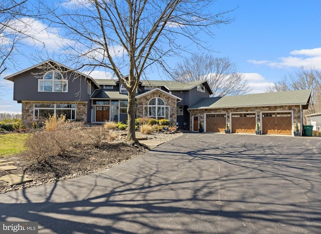 view of front facade with stone siding, an attached garage, and driveway