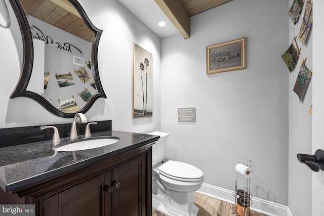 half bath featuring vanity, wood finished floors, visible vents, baseboards, and toilet