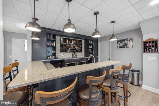 bar with light wood-type flooring, baseboards, wet bar, a paneled ceiling, and hanging light fixtures