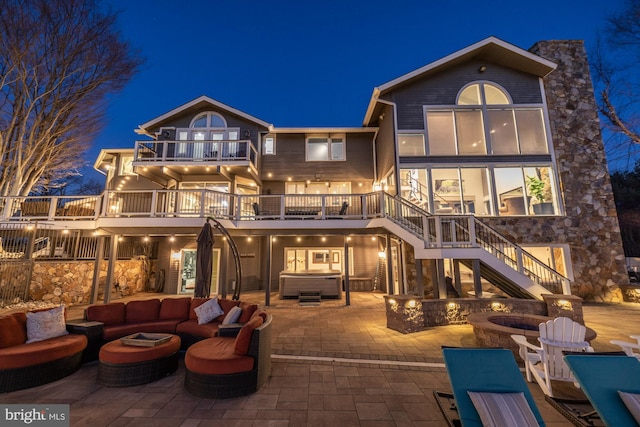 back of house at twilight featuring a patio, an outdoor living space with a fire pit, a balcony, stairs, and a hot tub