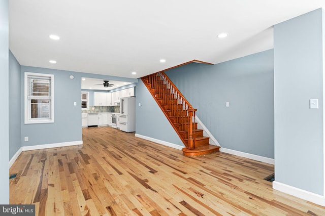 unfurnished living room featuring stairway, a ceiling fan, baseboards, light wood-style flooring, and recessed lighting