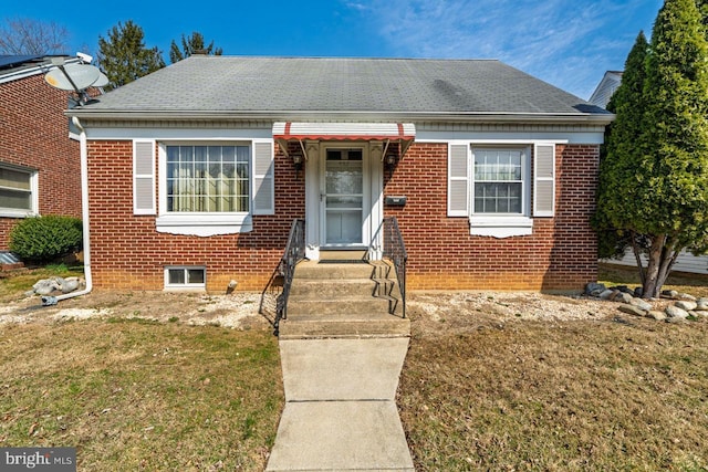 bungalow featuring brick siding, a front yard, and a shingled roof