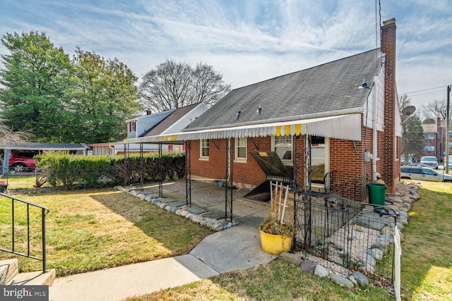 back of house with fence, roof with shingles, a yard, a chimney, and brick siding