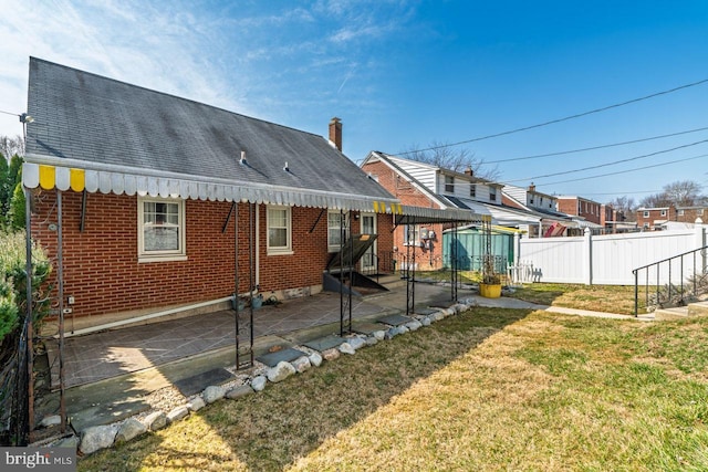 rear view of house featuring a patio, fence, roof with shingles, a yard, and brick siding