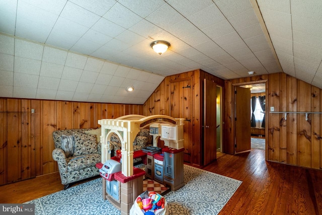 playroom featuring vaulted ceiling, wooden walls, and hardwood / wood-style floors