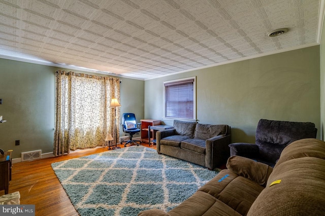 living room featuring visible vents, wood finished floors, baseboards, and ornamental molding