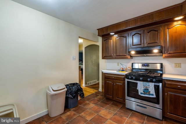 kitchen with visible vents, arched walkways, light countertops, under cabinet range hood, and stainless steel gas range oven