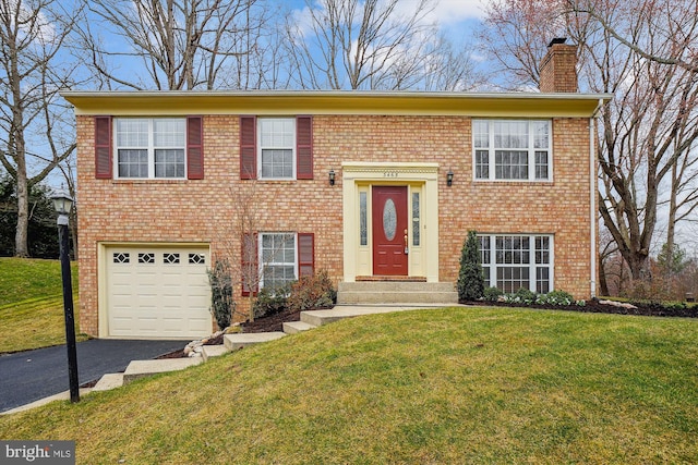 raised ranch with a front yard, brick siding, an attached garage, and driveway