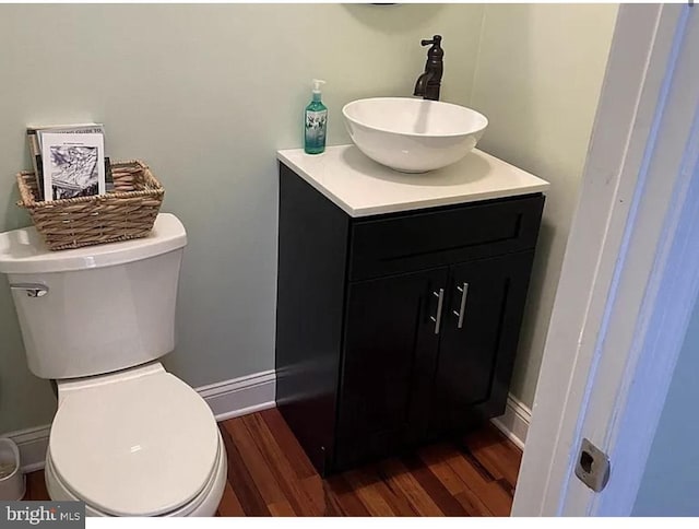 bathroom featuring baseboards, toilet, wood finished floors, and vanity