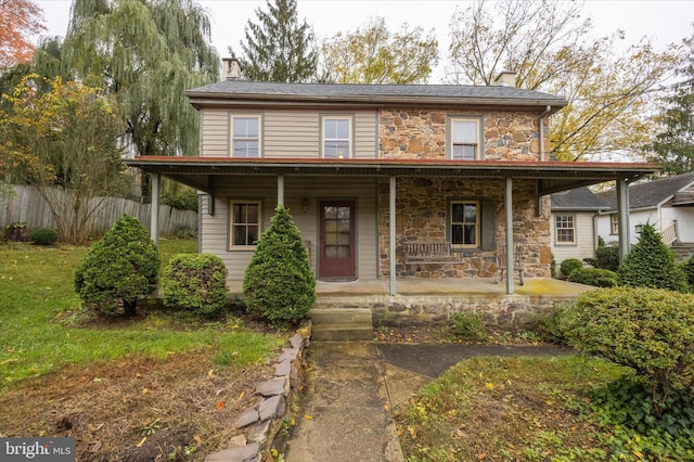 view of front of home with stone siding, a porch, a chimney, and fence