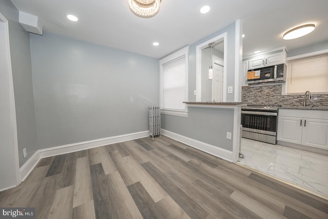 kitchen with radiator, backsplash, appliances with stainless steel finishes, and white cabinets