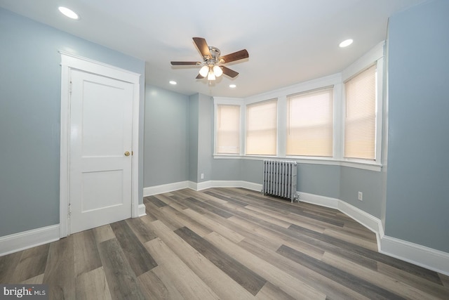 empty room featuring radiator heating unit, wood finished floors, baseboards, and ceiling fan