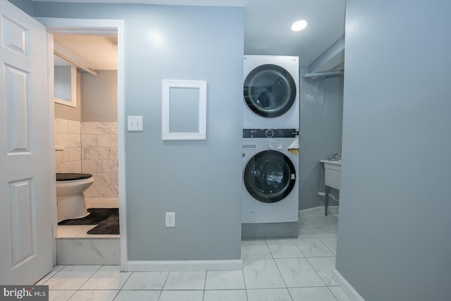 laundry room featuring laundry area, marble finish floor, stacked washer and clothes dryer, and baseboards