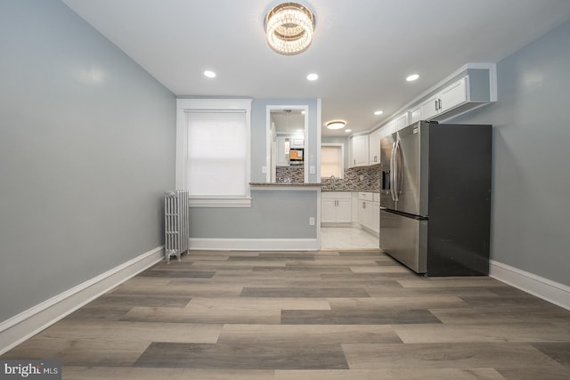 kitchen featuring stainless steel refrigerator with ice dispenser, backsplash, radiator, white cabinets, and baseboards