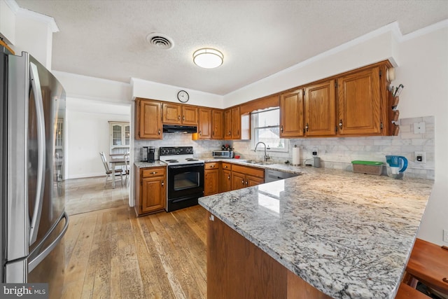 kitchen featuring visible vents, under cabinet range hood, a peninsula, stainless steel appliances, and a sink