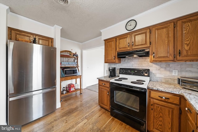 kitchen with tasteful backsplash, under cabinet range hood, brown cabinets, light wood-style floors, and stainless steel appliances