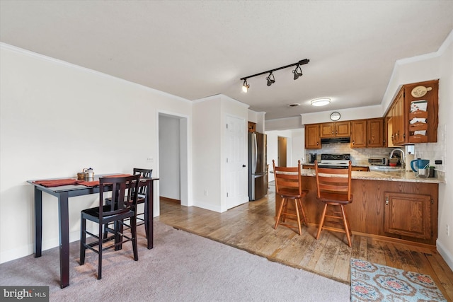 kitchen with brown cabinets, under cabinet range hood, freestanding refrigerator, crown molding, and decorative backsplash