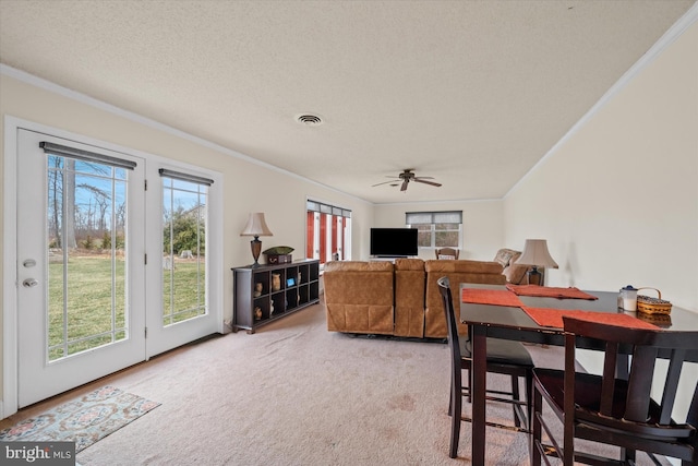 carpeted dining space with visible vents, a textured ceiling, crown molding, and a ceiling fan