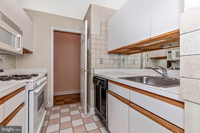 kitchen with wallpapered walls, light countertops, white cabinets, white appliances, and a sink