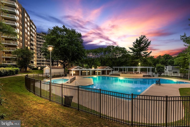 pool at dusk with a patio, a community pool, fence, and a yard