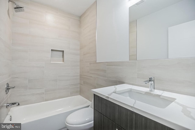 bathroom featuring vanity, visible vents, bathing tub / shower combination, tile walls, and toilet