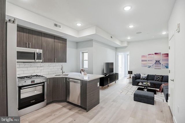 kitchen with dark brown cabinetry, open floor plan, appliances with stainless steel finishes, a peninsula, and a sink