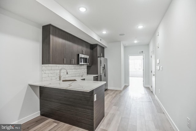 kitchen featuring baseboards, light wood finished floors, a sink, decorative backsplash, and appliances with stainless steel finishes