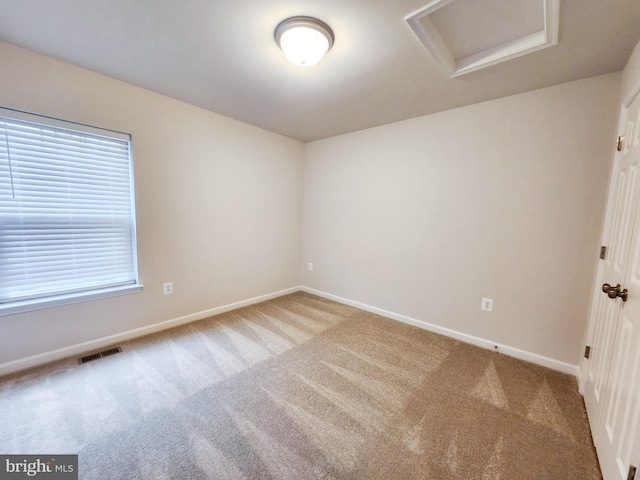 carpeted spare room featuring attic access, visible vents, and baseboards