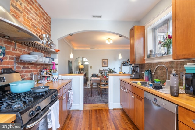 kitchen featuring visible vents, appliances with stainless steel finishes, exhaust hood, arched walkways, and a sink