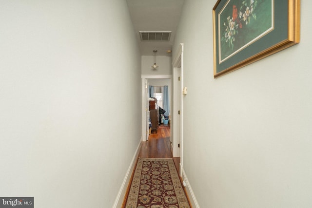 corridor featuring visible vents, baseboards, and wood finished floors