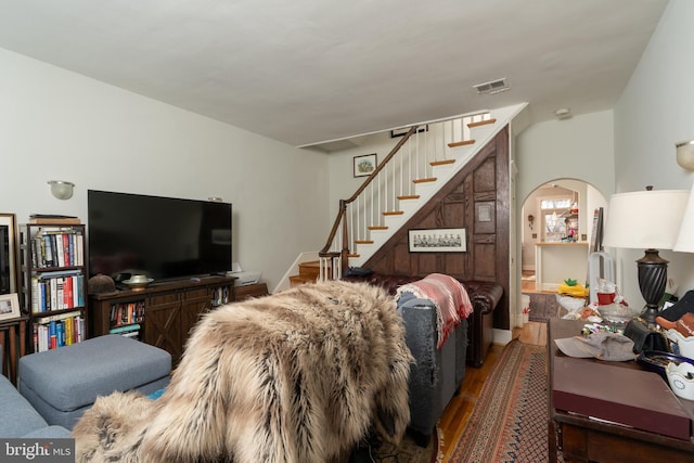 living room with visible vents, wood finished floors, arched walkways, baseboards, and stairs