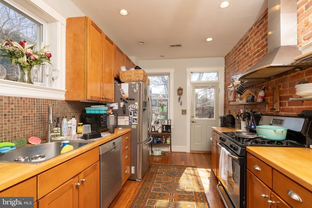 kitchen featuring visible vents, dark wood finished floors, a sink, appliances with stainless steel finishes, and wall chimney range hood