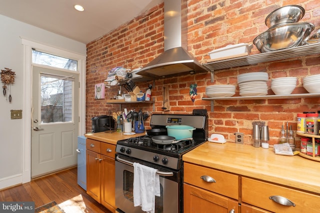 kitchen with stainless steel gas range oven, light wood finished floors, brick wall, wall chimney range hood, and butcher block counters