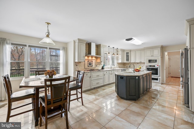 kitchen featuring stainless steel appliances, a sink, decorative light fixtures, wall chimney exhaust hood, and decorative backsplash