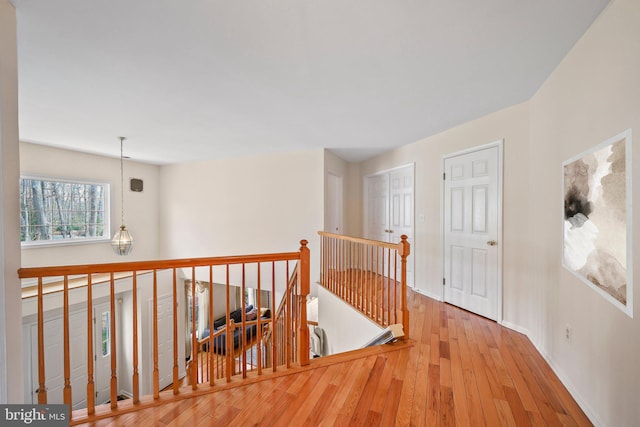 corridor featuring wood-type flooring, baseboards, and an upstairs landing