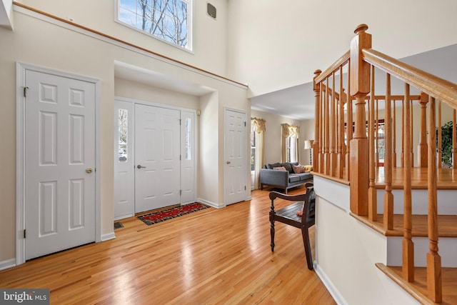 entryway featuring stairway, baseboards, a high ceiling, and light wood-style flooring
