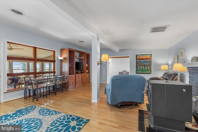 living room with light wood finished floors, visible vents, beam ceiling, and baseboards