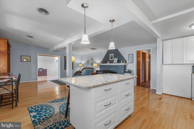 kitchen with visible vents, a brick fireplace, white cabinetry, and light wood-style floors