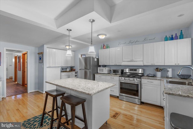 kitchen featuring under cabinet range hood, light wood-style floors, appliances with stainless steel finishes, and a sink