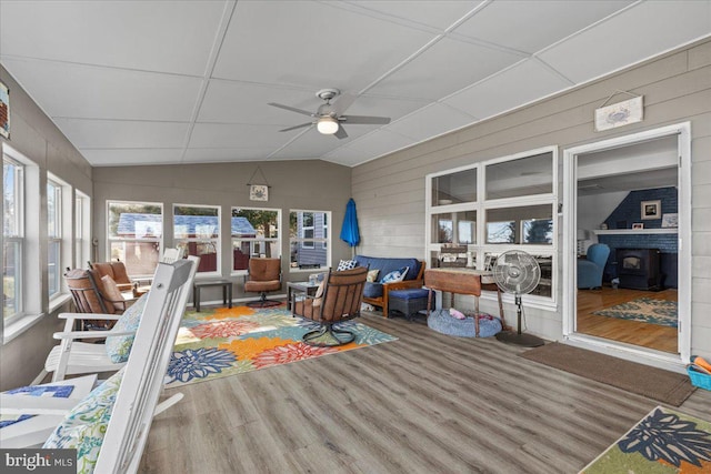 sunroom / solarium with lofted ceiling, a wood stove, and ceiling fan