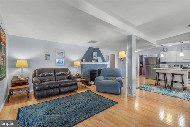 living room with visible vents, a brick fireplace, baseboards, a toaster, and light wood-type flooring