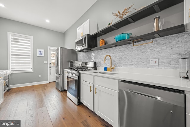 kitchen with light wood-type flooring, a sink, open shelves, appliances with stainless steel finishes, and decorative backsplash