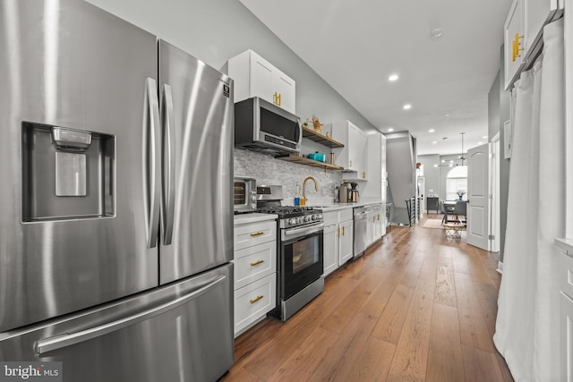 kitchen featuring light wood-type flooring, white cabinetry, appliances with stainless steel finishes, light countertops, and decorative backsplash