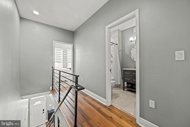 hall featuring wood finished floors, an upstairs landing, and baseboards