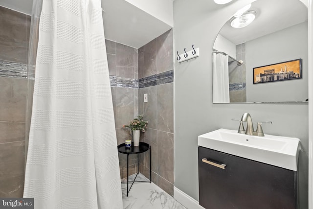 bathroom featuring baseboards, tiled shower, marble finish floor, and vanity