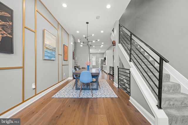 unfurnished dining area with stairs, an inviting chandelier, recessed lighting, and wood finished floors