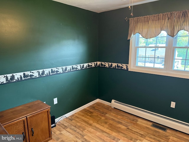 spare room featuring baseboards, a baseboard heating unit, and wood finished floors