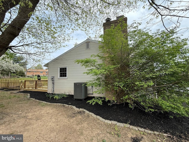 view of side of property featuring cooling unit, a chimney, and a wooden deck