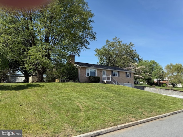 view of front facade featuring a garage, a front yard, a chimney, brick siding, and driveway